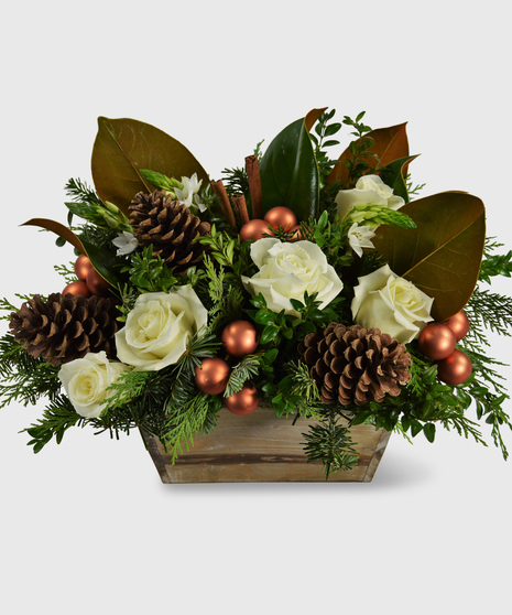 Magnolia leaves, white roses, copper balls, pine cones and lush holiday greens designed in a brown wooden box