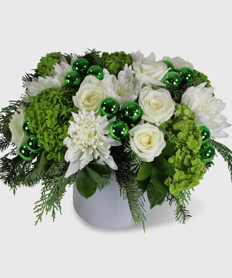 A green and white holiday arrangement designed in a white cylinder vase
