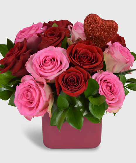 One dozen red and pink roses designed in a square pink vase with a heart pick