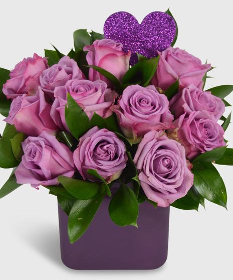 One dozen purple roses designed in a square purple vase with a heart pick