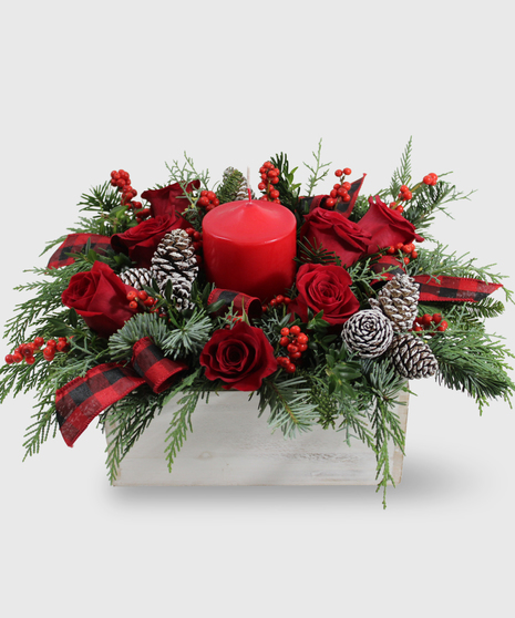 A winter centerpiece of red flowers, ribbons and pinecones in a white wooden box adorned with a white candle
